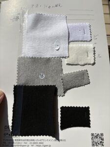 自然の太陽光下で白のカットソー身頃生地と2種類のリブ生地（c/#15とc/#32）の色差を比較し黄色みのリブ（c/#32）が馴染んでいる状態を示すスワッチ台紙の写真