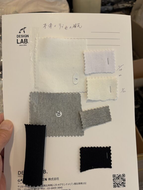 室内昼白色ライト下で白のカットソー身頃生地と2種類のリブ生地(c/#15とc/#32)の色馴染みを比較しているスワッチ台紙の写真
